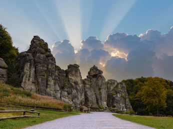 Felsformation im Teutoburger Wald, umgeben von Wald und Wiesen, unter strahlendem Himmel.