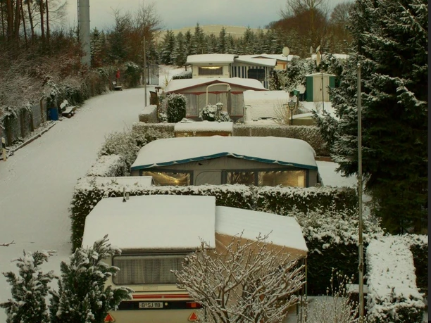 Campingplatz Am Waldschwimmbad_Winter Verschneiter Campingplatz mit Wohnwagen und Hütten, umgeben von Schneebäumen und ruhiger Natur.
