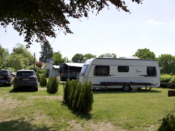Campingplatz Badeinsel Ernst und Christa Pfaff Ein Campingplatz mit einem Wohnwagen und mehreren Autos auf einer grünen Wiese, die von Bäumen und Sträuchern umgeben ist.