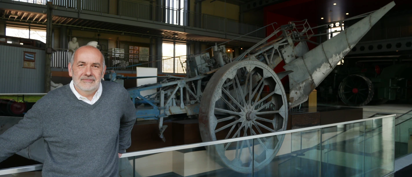 Historiker Ansgar Becker in der Ausstellungshalle II, die die Geschichte des Emslandplans ab 1950 beherbergt. Historiker steht vor landwirtschaftlicher Maschine in moderner Ausstellungshalle zum Emslandplan.