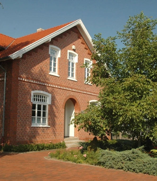 Landwirtschaftsmuseum Rhede (Ems) ©Gemeinde Rhede (Ems) .JPG Backsteingebäude mit rotem Dach, umgeben von Bäumen, Blumenbeeten und dem Schild des Landwirtschaftsmuseums.