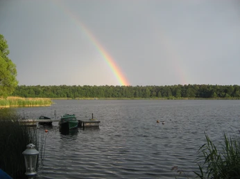 Campingplatz am Gudower See_Blick auf See Ein See mit kleinen Booten am Steg. Am Horizont ein Wald und ein leuchtender Regenbogen am Himmel.