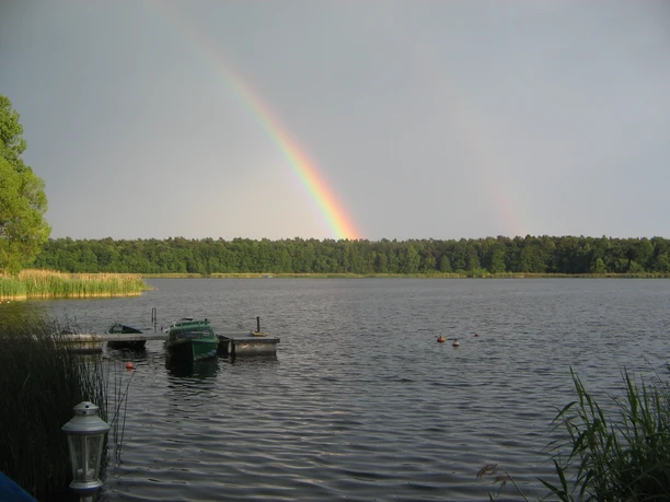 Campingplatz am Gudower See_Blick auf See Ein See mit kleinen Booten am Steg. Am Horizont ein Wald und ein leuchtender Regenbogen am Himmel.