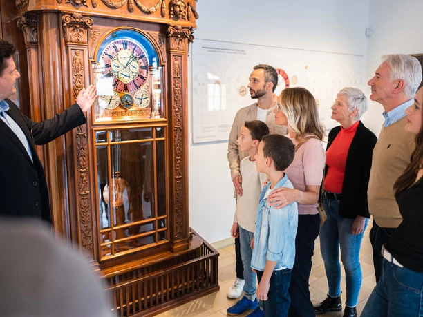 Führung Uhrenmuseum Gruppe betrachtet antike Standuhr im Uhrenmuseum, geführt von einem Mann.