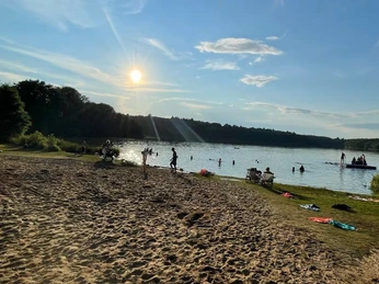 Camping- und Mobilheim am Lütauer See_Badestelle Eine Badestelle am Lütauer See mit sandigem Ufer, Menschen im Wasser und im Hintergrund bewaldete Ufer.