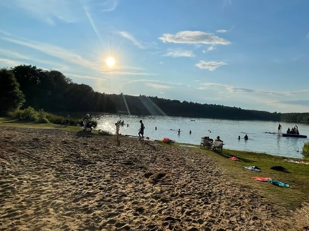 Camping- und Mobilheim am Lütauer See_Badestelle Eine Badestelle am Lütauer See mit sandigem Ufer, Menschen im Wasser und im Hintergrund bewaldete Ufer.