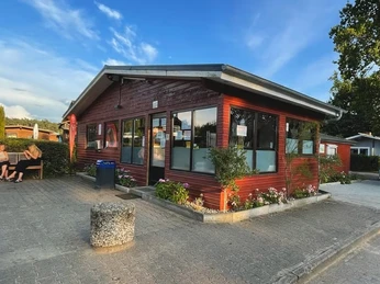 Camping- und Mobilheim am Lütauer See_Mobilheim Ein rotes Mobilheim mit Fenstern steht auf einem gepflasterten Platz, umgeben von Bäumen und Blumen.