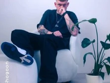 Ein junger Mann sitzt lässig in einem Sessel, neben ihm eine Pflanze in einem weißen Raum.