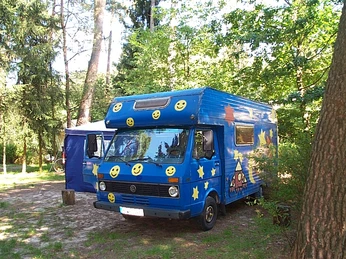 Schaalsee-Camp Wohnmobil umgeben von Bäumen auf einem Campingplatz, blau mit gelben Smileys und Sternen bemalt.