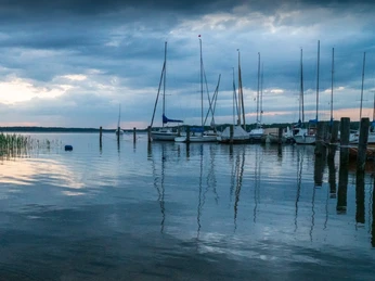 Naturcamping Buchholz_Segelboote Boote liegen an einem ruhigen See bei bewölktem Himmel.