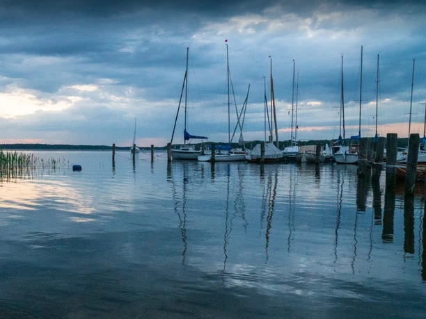 Naturcamping Buchholz_Segelboote Boote liegen an einem ruhigen See bei bewölktem Himmel.