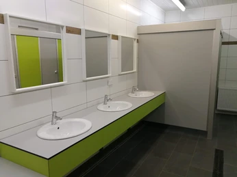 Naturcamping Buchholz_Sanitär Drei weiße Waschbecken mit Spiegeln, grüne Details und ein moderner, sauberer Sanitärbereich im Campingplatz.