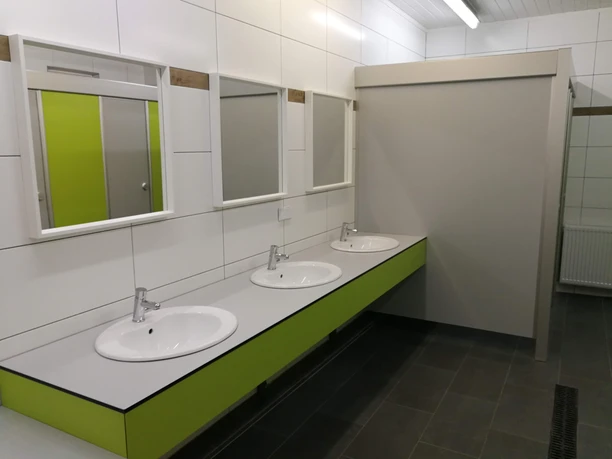 Naturcamping Buchholz_Sanitär Drei weiße Waschbecken mit Spiegeln, grüne Details und ein moderner, sauberer Sanitärbereich im Campingplatz.