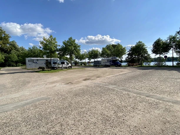 Wohnmobilstellplatz Geesthacht_Stellplätze Zwei Wohnmobile stehen auf einem Parkplatz, umgeben von Bäumen und einem klaren blauen Himmel.