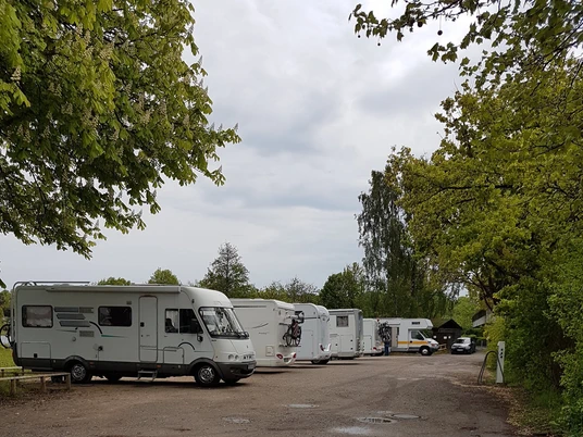 Wohnmobilstellplatz Ratzeburg_Stellplätze Reihe geparkter Wohnmobile auf einem Stellplatz, umgeben von Bäumen und Wolken am Himmel.