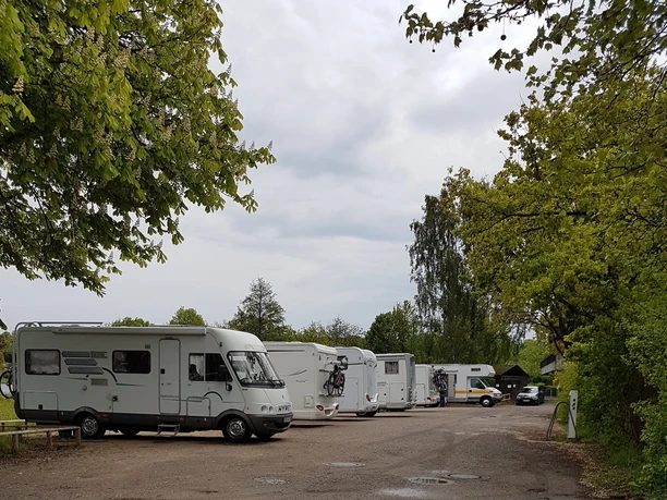 Wohnmobilstellplatz Ratzeburg_Stellplätze Reihe geparkter Wohnmobile auf einem Stellplatz, umgeben von Bäumen und Wolken am Himmel.