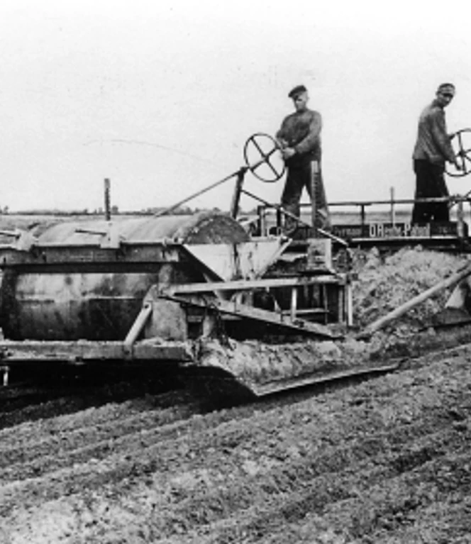 Um eine ebene Oberfläche für den späteren Ackerboden zu bekommen, mussten die gepflügten Flächen mittels eines entsprechenden Erdhobels geebnet werden. Drei Arbeiter bedienen einen Erdhobel, der gepflügte Moorflächen zu ebenem Ackerboden glättet.