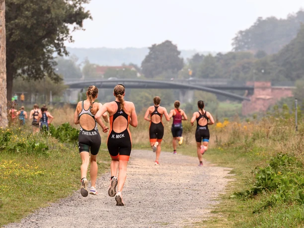1 - Muldental Triathlon - Foto Matthias Vogel.png Triathleten laufen auf einem weiten Pfad, von Bäumen und Landschaft umgeben, Richtung Brücke.