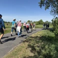 IMG_8688.JPG Group of hikers in outdoor clothing walking on an asphalt path through a green landscape in sunny weather.