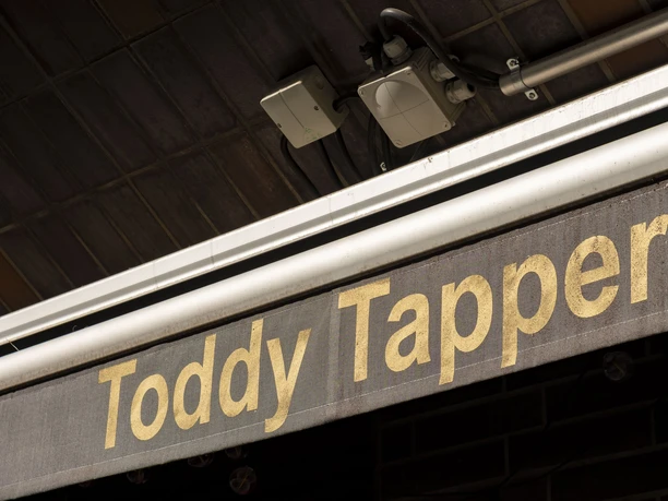 Toddy Tapper A sign with the inscription 'Toddy Tapper' in gold lettering against a dark background structure.