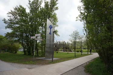 Freizeitpark Nordstadt an der Höferstraße in Velbert-Mitte Großer Freizeitpark mit Holzspielplatz, gepflasterten Wegen vor üppigen Bäumen und moderner Skulptur.