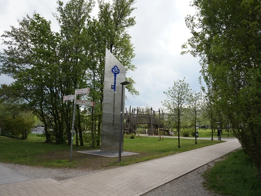 Freizeitpark Nordstadt an der Höferstraße in Velbert-Mitte Großer Freizeitpark mit Holzspielplatz, gepflasterten Wegen vor üppigen Bäumen und moderner Skulptur.