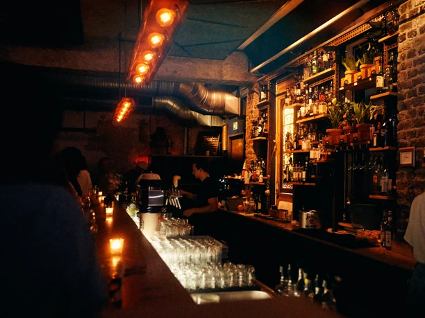 Bumann und Sohn Ein stilvolles, atmosphärisches Bar-Setting mit gedämpften Lichtern, voll bestückten Regalen und freundlichem Personal.