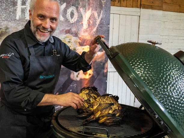 FIRE&FOOD BBQ WEEK A friendly chef proudly presents two grilled cabbages on a large green grill.