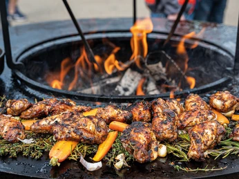 FIRE&FOOD BBQ WEEK Grilled chicken thighs and vegetables on fresh herbs over an open fire, flames blazing.