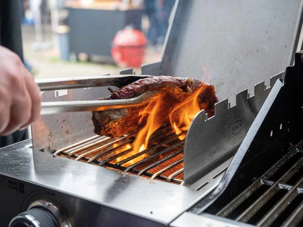 FIRE&FOOD BBQ WEEK A juicy steak is turned with tongs on a grill and roasted over an open flame.