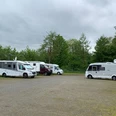 Wohnmobilstellplatz Mölln_Stellplätze Der Wohnmobilstellplatz Mölln bietet einen offenen Schotterplatz mit mehreren parkenden Wohnmobilen. Bäume umranden den Platz.
