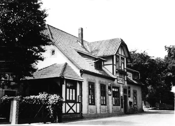 Das Pfarrwitwenhaus Alte Apotheke Historisches Gebäude mit Fachwerkdetails und markantem Giebeldach, vorne Bäume und Gehweg.