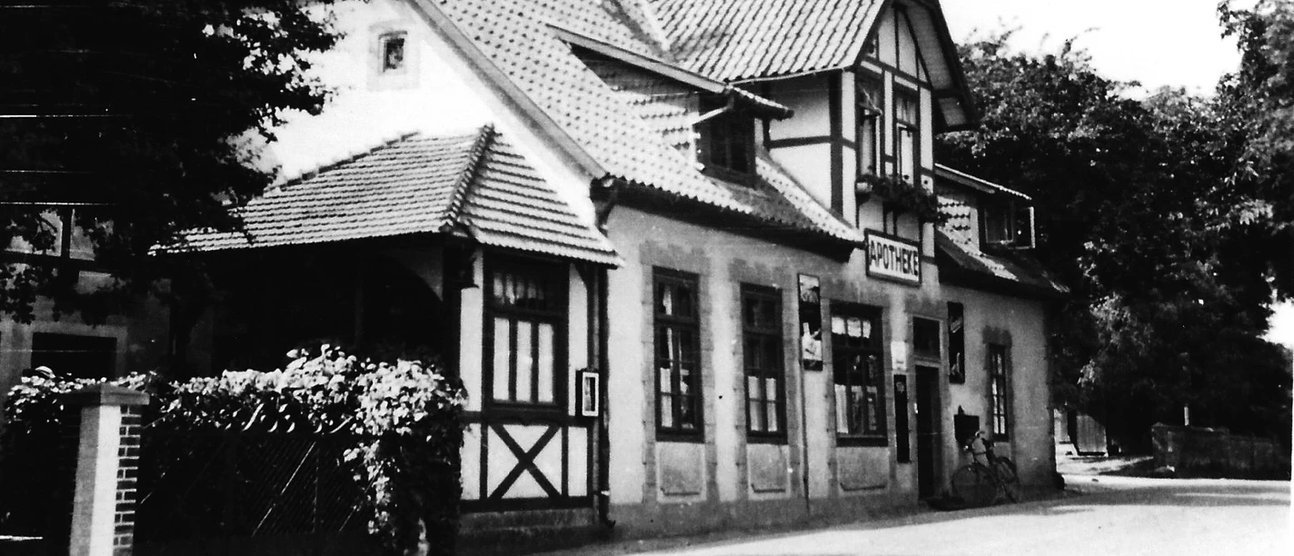 Das Pfarrwitwenhaus Alte Apotheke Historisches Gebäude mit Fachwerkdetails und markantem Giebeldach, vorne Bäume und Gehweg.