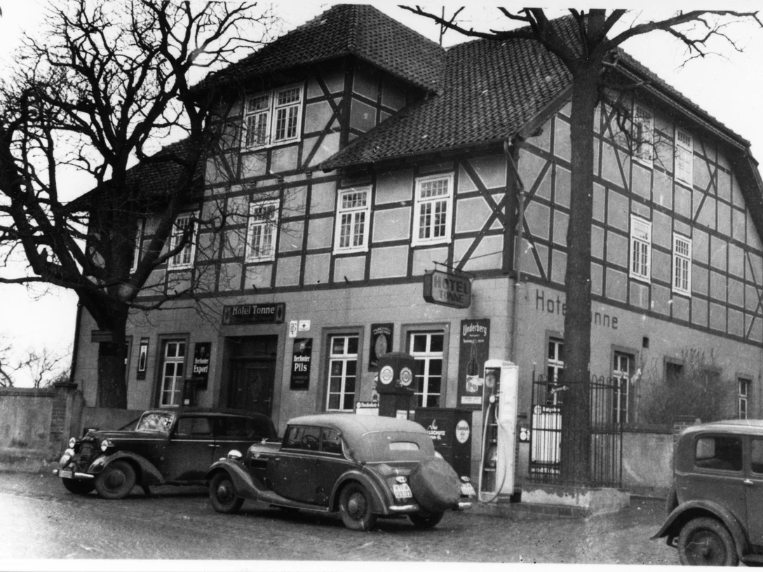 Hotel Tonne Historisches Fachwerkgebäude mit antiken Autos davor; das Hotel Tonne-Logo ziert die Wand.