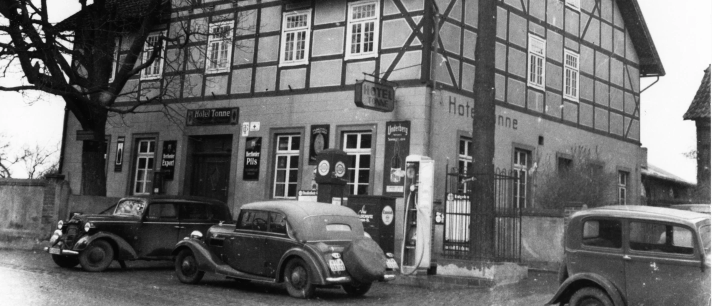 Hotel Tonne Historisches Fachwerkgebäude mit antiken Autos davor; das Hotel Tonne-Logo ziert die Wand.
