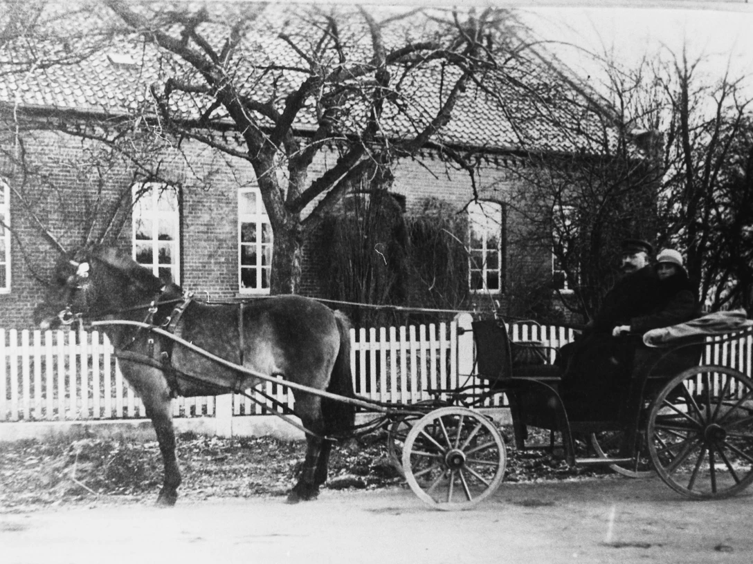 Altes Amtshaus Historische Pferdekutsche vor einem Backstein-Gebäude mit weißen Fenstern und Holzzaun.