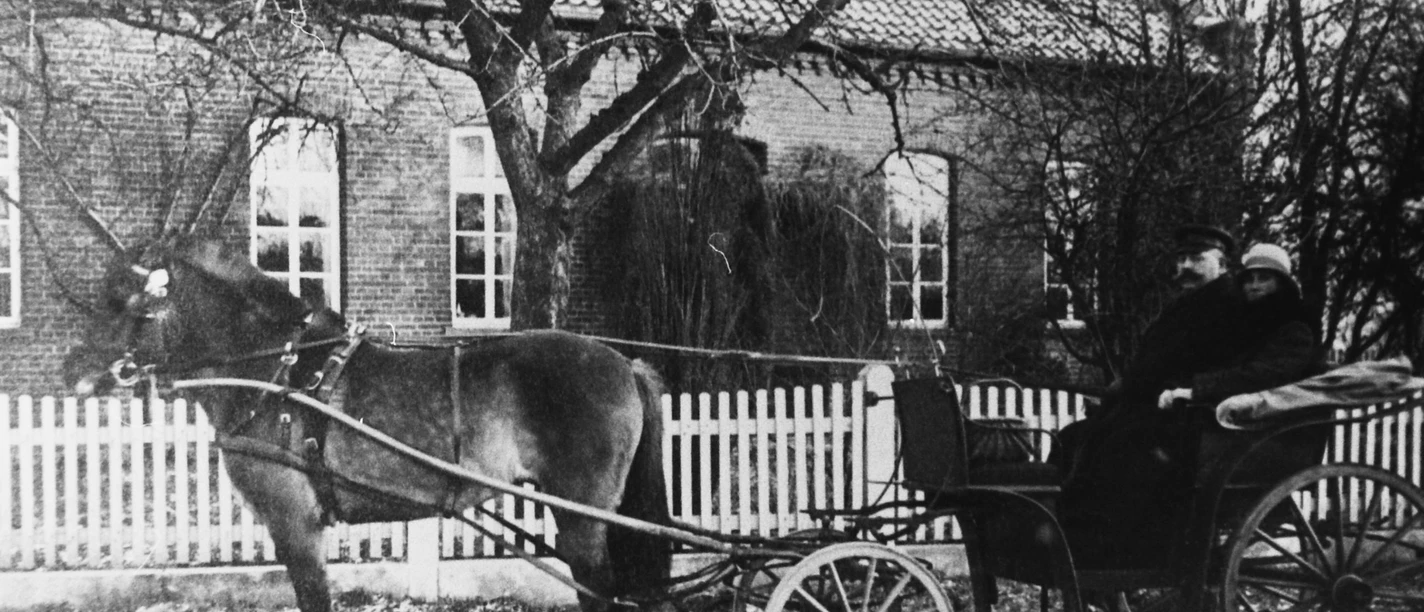 Altes Amtshaus Historische Pferdekutsche vor einem Backstein-Gebäude mit weißen Fenstern und Holzzaun.