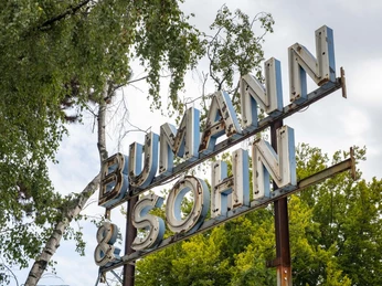 Bumann & Sohn Ein Metall-Schild mit der Aufschrift "Bumann & Sohn" erhebt sich gegen den bewölkten Himmel.A metal sign with the inscription "Bumann & Sohn" rises up against the cloudy sky.