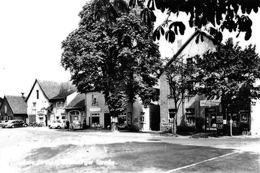 Köhnen Ecke Schwarzweiß-Foto einer Straßenecke mit alten Gebäuden, Autos, großen Bäumen und einem Ladengeschäft.