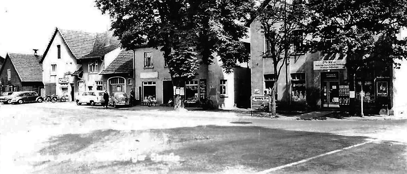 Köhnen Ecke Schwarzweiß-Foto einer Straßenecke mit alten Gebäuden, Autos, großen Bäumen und einem Ladengeschäft.