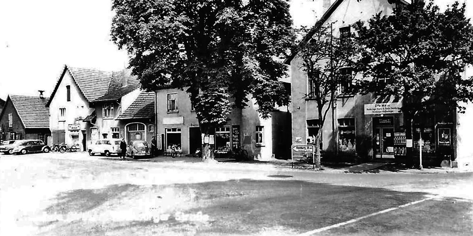 Köhnen Ecke Schwarzweiß-Foto einer Straßenecke mit alten Gebäuden, Autos, großen Bäumen und einem Ladengeschäft.