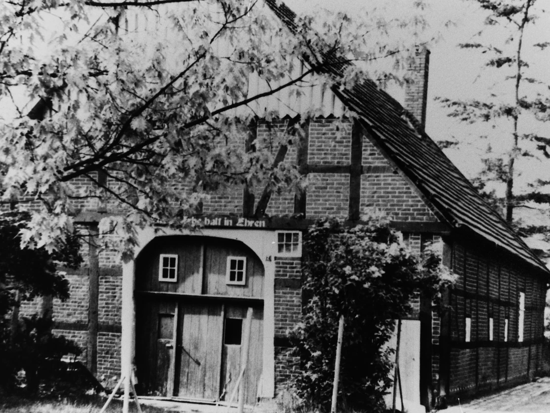 Küsterhaus Altes Fachwerkhaus mit steilem Dach und hölzernen Toren, umgeben von blühenden Bäumen und Sträuchern.
