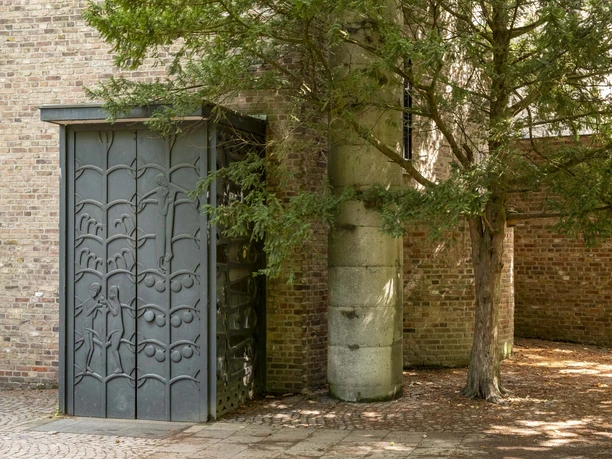 St. Alban A modern building façade with a filigree metal element and the shade of a large conifer.