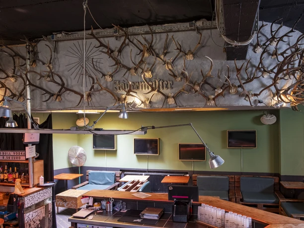 artheater Interior of the Artheater, decorated with numerous deer antlers on the ceiling. The antlers are mounted at regular intervals and give the room a rustic flair. A bar and various seating options can be seen in the foreground. The room radiates a creative and unique atmosphere thanks to the arrangement of the elements.