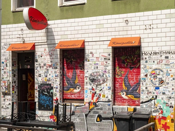 Königsblut Die Außenwand eines Lokals in Köln ist übersät mit Stickern und bunten Graffiti, an zwei roten Markisen hängt der Schriftzug "Königsblut".