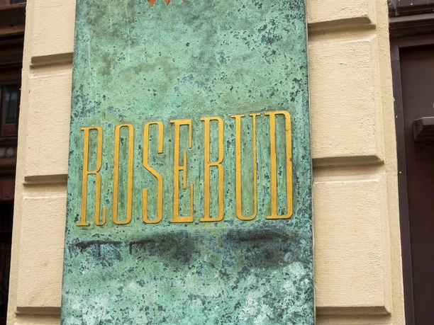 Rosebud Ein großes, türkisfarbenes Wandrelief mit dem Schriftzug "Rosebud" in goldener Farbe ziert die Fassade.