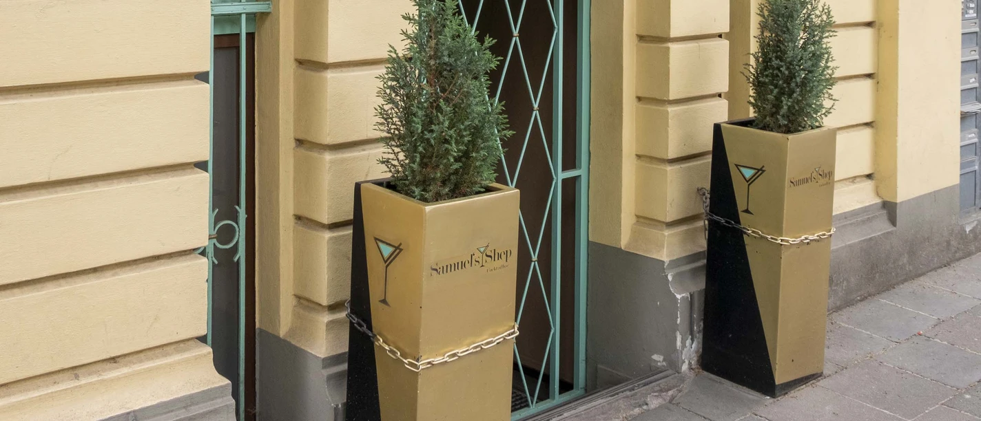 Samuels Shep Die Fassade eines Gebäudes mit großen Fenstern und zwei modernen Pflanzgefäßen flankiert den Eingang.