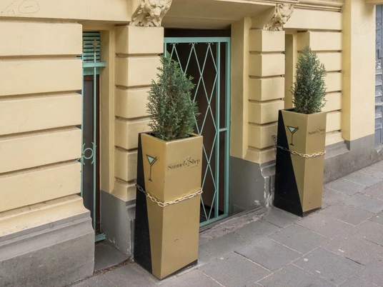 Samuels Shep Die Fassade eines Gebäudes mit großen Fenstern und zwei modernen Pflanzgefäßen flankiert den Eingang.The façade of a building with large windows and two modern planters flanks the entrance.