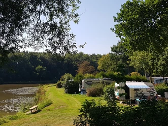 1_kcp_haren_20210909_130629_schnitt.jpg Grüne Uferwiese mit Wohnwagen am See, umgeben von Bäumen, bei sonnigem, klarem Sommerwetter.