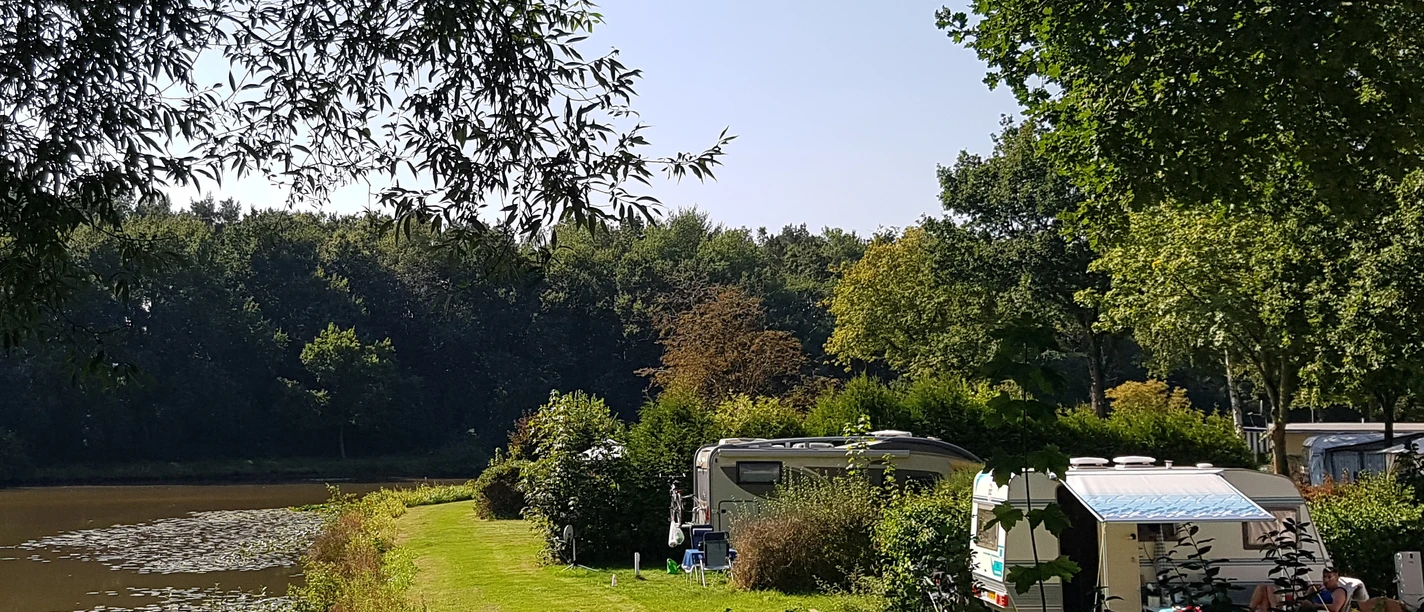 1_kcp_haren_20210909_130629_schnitt.jpg Grüne Uferwiese mit Wohnwagen am See, umgeben von Bäumen, bei sonnigem, klarem Sommerwetter.